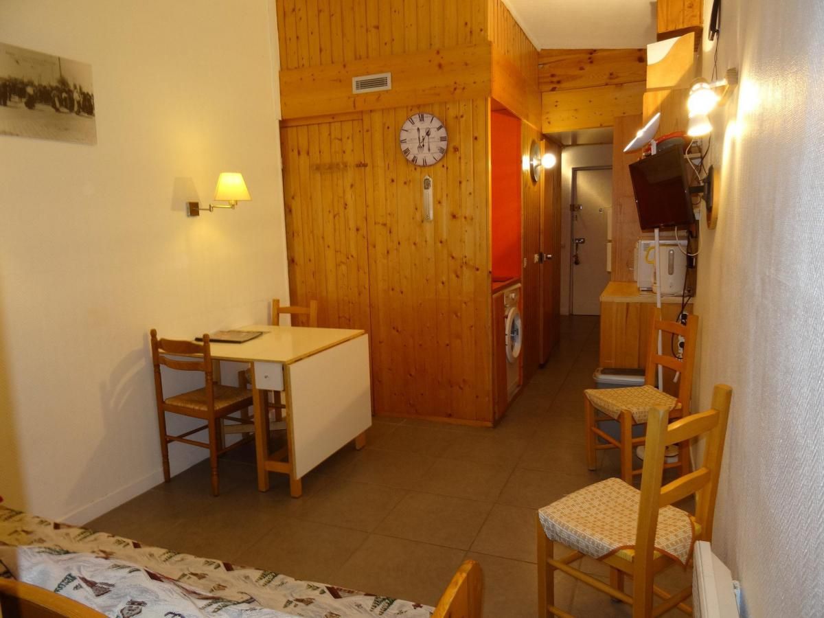 A compact room with a wooden dining table, two chairs, a washing machine, and a clock on the wall.