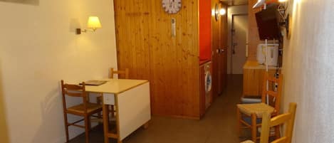 A compact room with a wooden dining table, two chairs, a washing machine, and a clock on the wall.