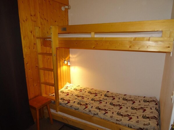 A bunk bed with a ladder and a small stool, a wall-mounted light, and a patterned bedspread.