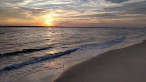 Ein Strand mit Sonnenuntergang über dem Wasser, sanfte Wellen umspülen das Ufer.