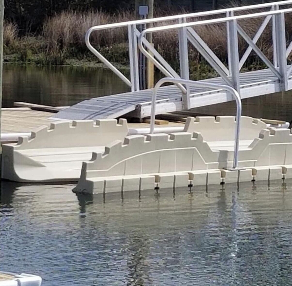 Un muelle de hormigón con barandilla metálica que se adentra en una masa de agua tranquila.