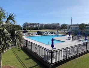 Una piscina rectangular con una cerca metálica negra, rodeada de césped y palmeras.