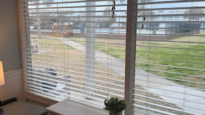 Ein Zimmer mit einem großen Fenster, das mit Jalousien verdeckt ist, einem kleinen Tisch mit einer Lampe und einer Klimaanlage auf der Fensterbank.