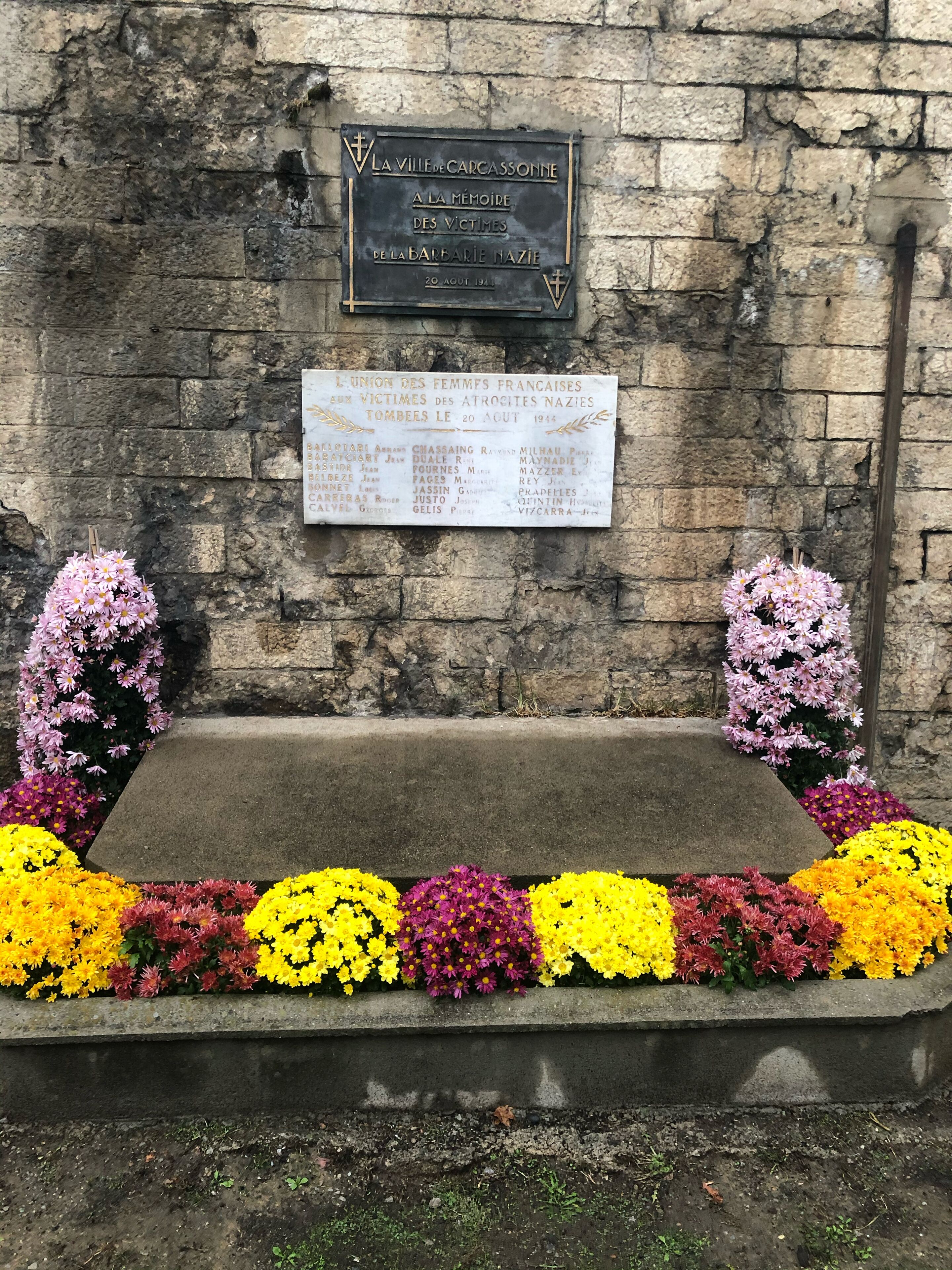 A memorial plaque on a stone wall with a list of names.