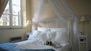 A bedroom with a canopy bed, white bedding, a bedside table with a lamp, and a window with curtains. - Carcassonne, elegant apartment overlooking central square (Carcassonne)