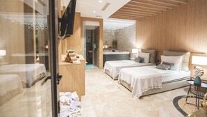 Ein modernes Hotelzimmer mit zwei Betten, einer Sitzecke, einer kleinen Küchenzeile und einem durchgehenden Tür einsehbaren Badezimmer.