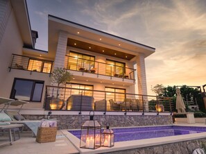 Une maison moderne à deux étages, dotée d’une piscine, d’un espace salon extérieur et d’un balcon bien éclairé.