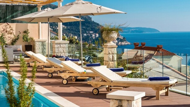 Zona de piscina con sillones de descanso, sombrillas y vista al mar.