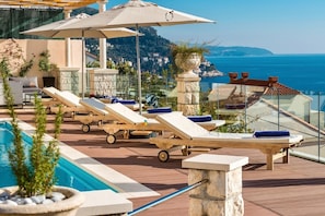 Un espace aménagé au bord de la piscine, avec des chaises longues, des parasols et une vue sur la mer.