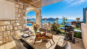 Un patio con paredes de piedra, mobiliario de mimbre, una mesa de madera con comida para el desayuno y una parrilla.