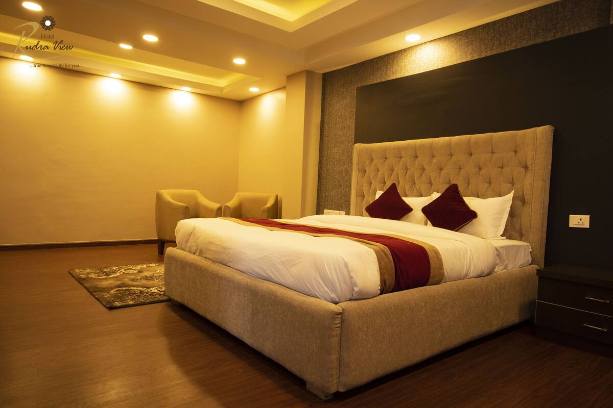 A hotel room with a large bed, a headboard, a bedside table, and a chair.
