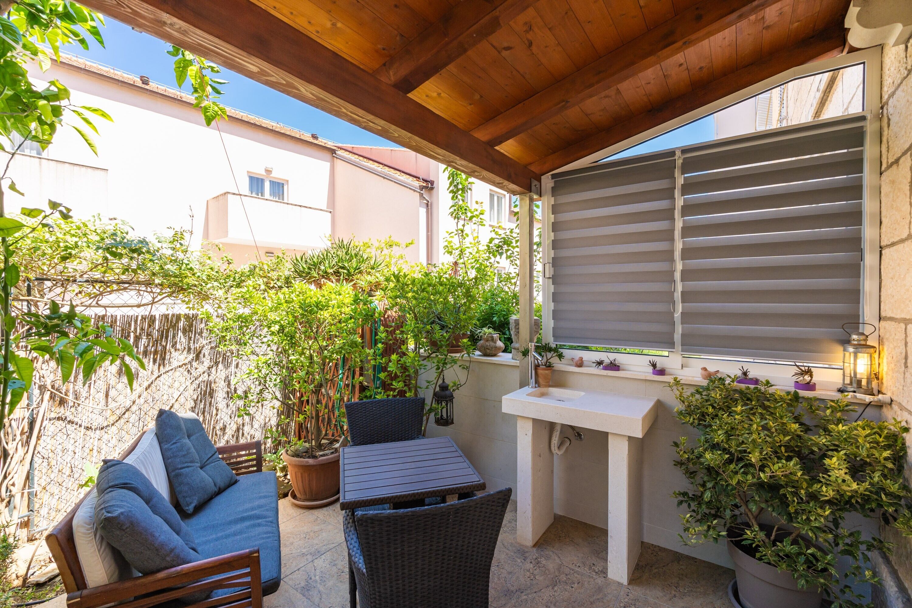 A covered patio with a sofa, table, and potted plants.