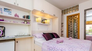 A bedroom with a bed, bedside table, and a desk with a computer. There is a window with a view of the outside. - Apartments and Room Frane - Double Room (Dubrovnik)