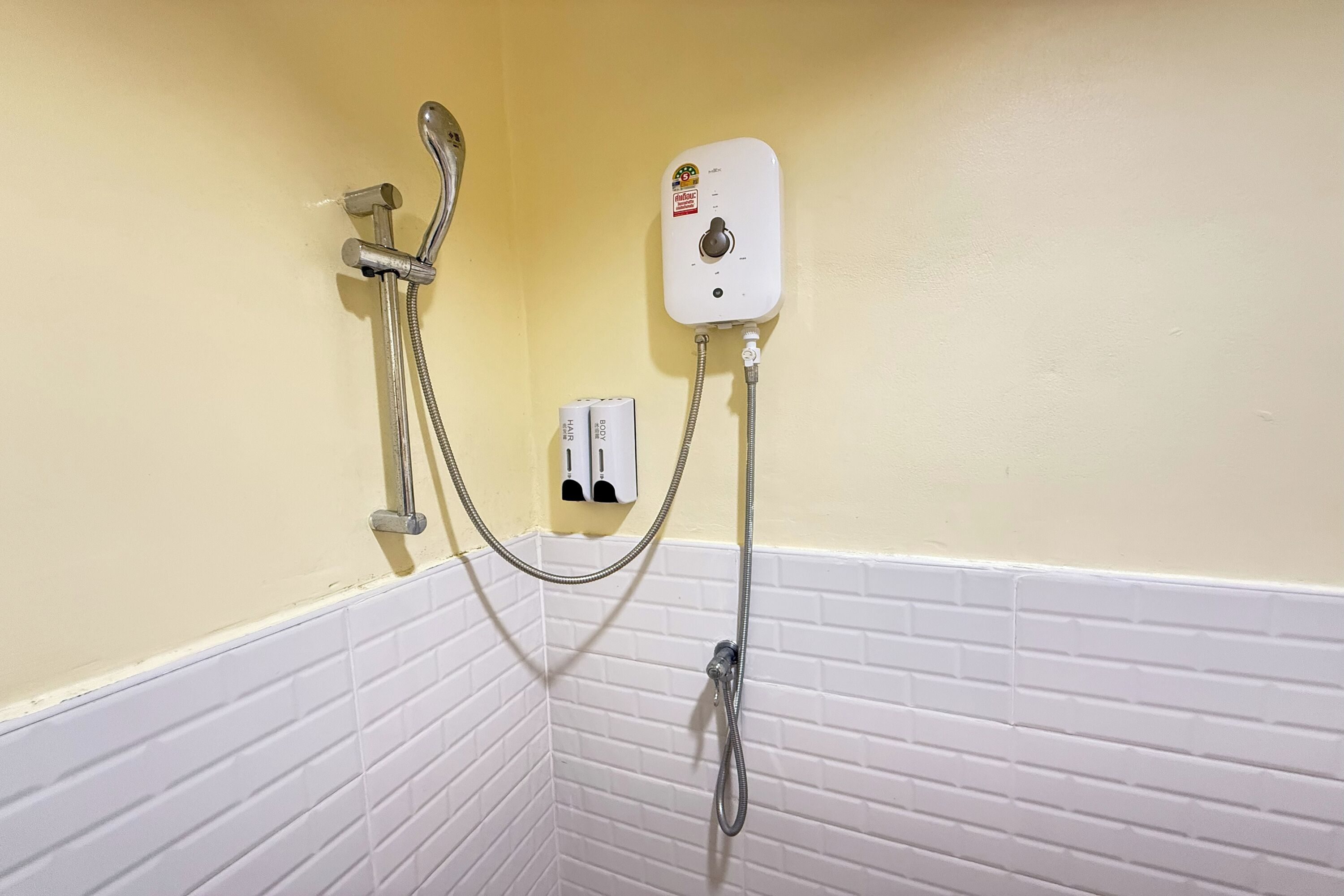 A bathroom with a shower, a hand dryer, and a wall-mounted control panel.