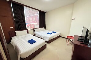 A hotel room with two single beds, a desk with a computer, and a window with curtains. - Scala Hostel (Bangkok)