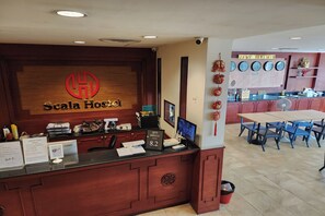 A hotel reception desk with a wooden counter, a sign reading "Scala Hotel," and a digital screen displaying the hotel's name. - Scala Hostel (Bangkok)