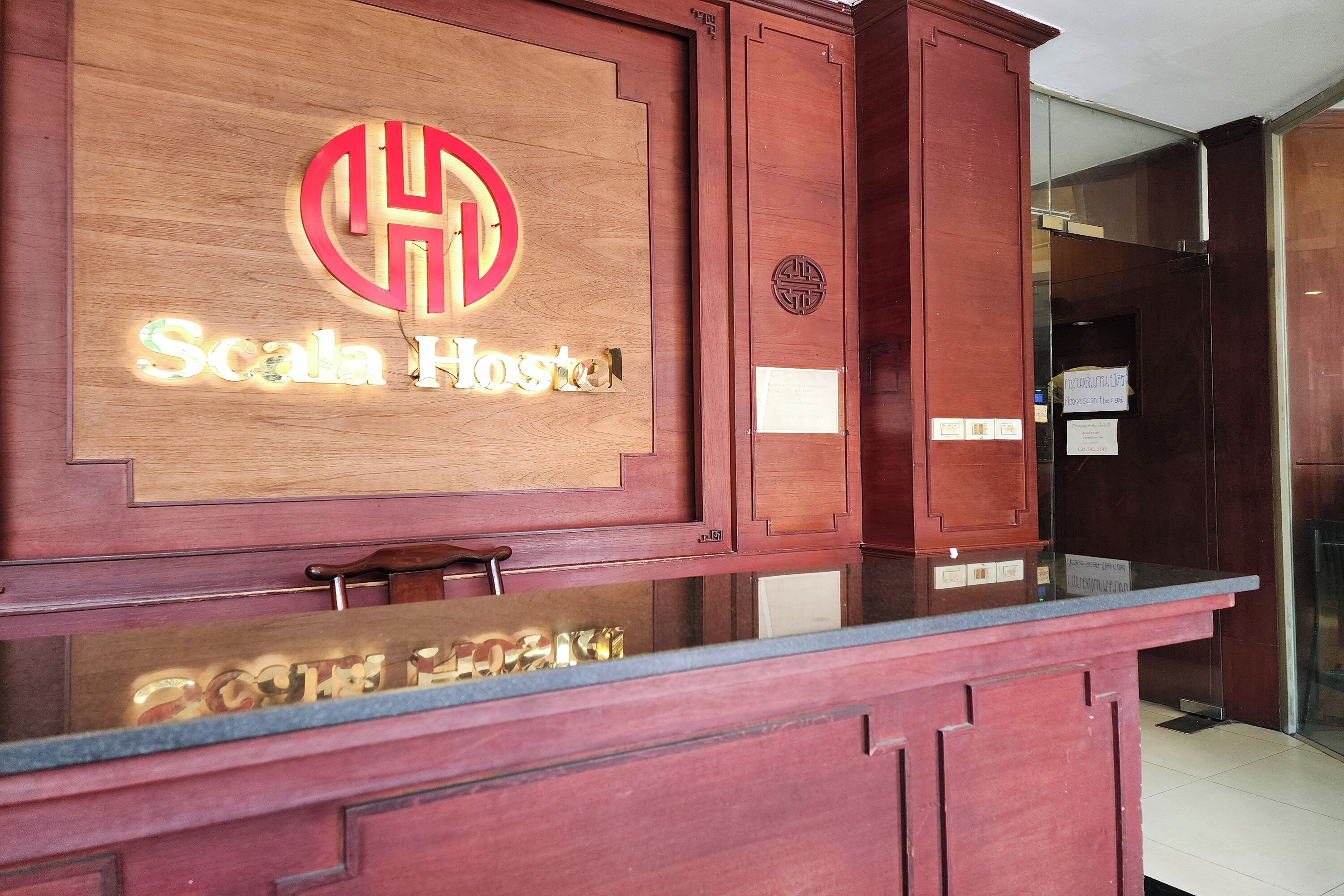 A reception desk with a wooden panel displaying the logo and name 'Scala Hostel'.