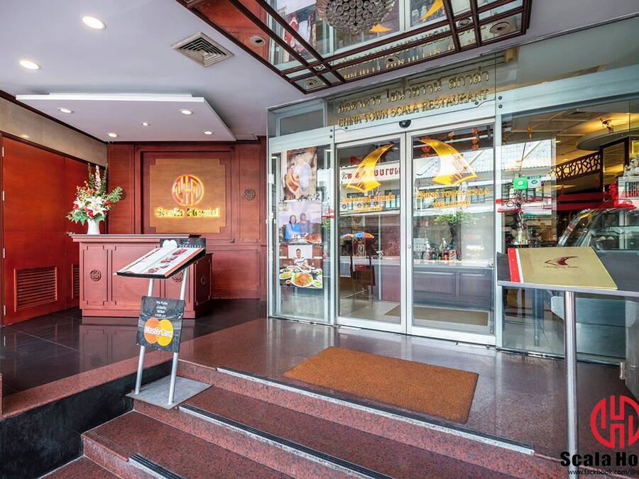 Un vestíbulo de hotel con una recepción, una escalera que sube al piso superior y un restaurante llamado "China Town Scala Restaurant" visible a través de puertas de vidrio.