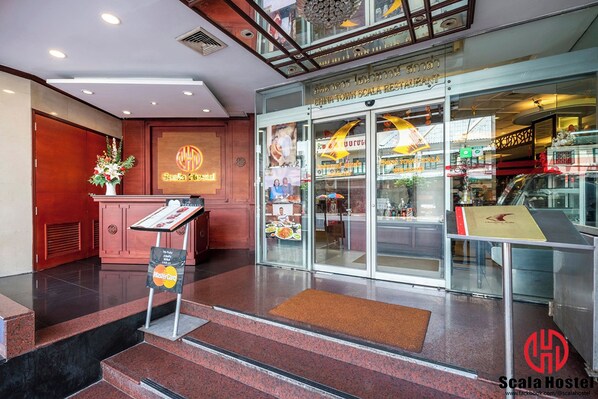 Eine Hotelhalle mit einer Rezeption, einer Treppe, die in die oberen Stockwerke führt, und einem Restaurant namens "China Town Scala Restaurant", das durch die Glastüren sichtbar ist.