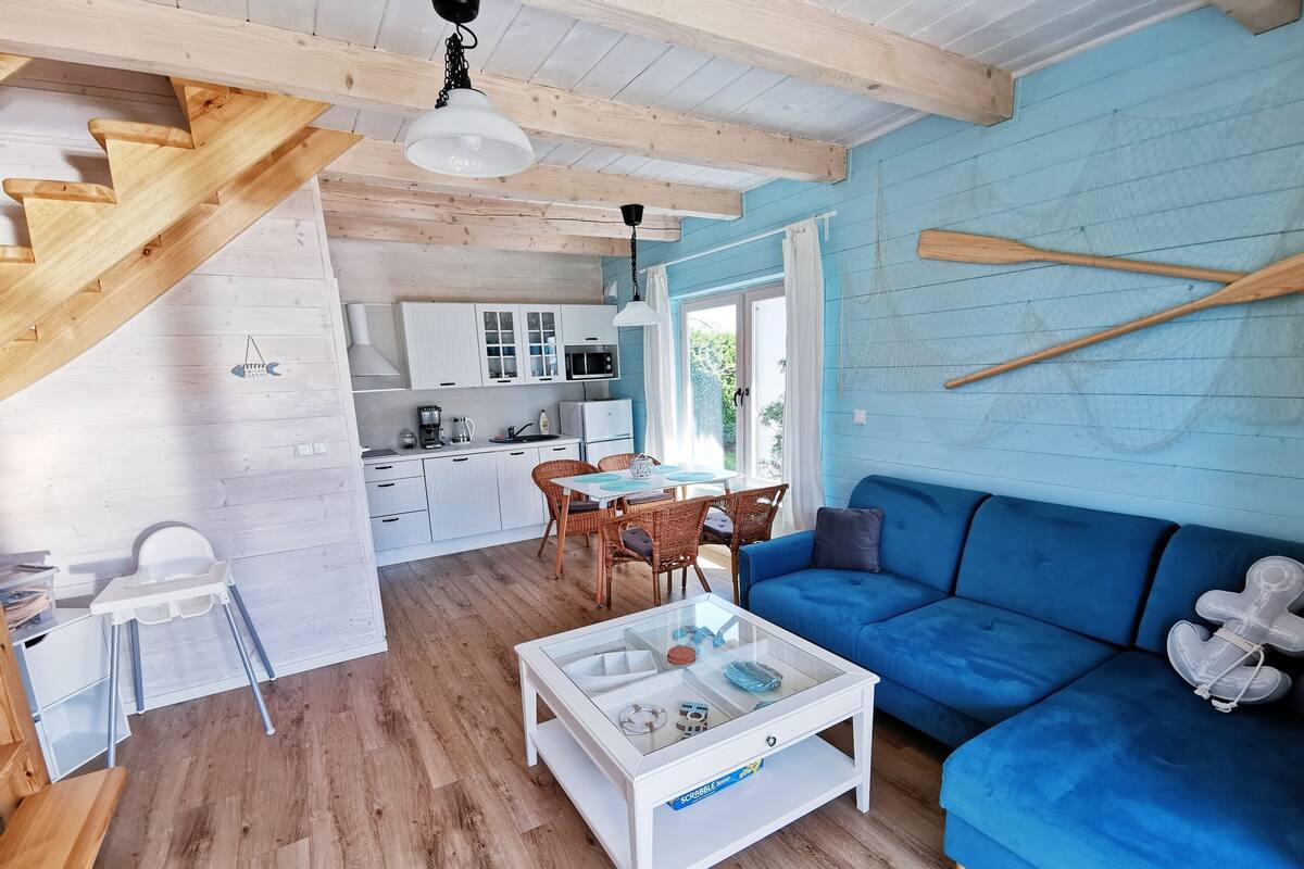 Een gezellige woonkamer met een blauwe bank, een glazen salontafel en een keuken met witte kasten en een eettafel.
