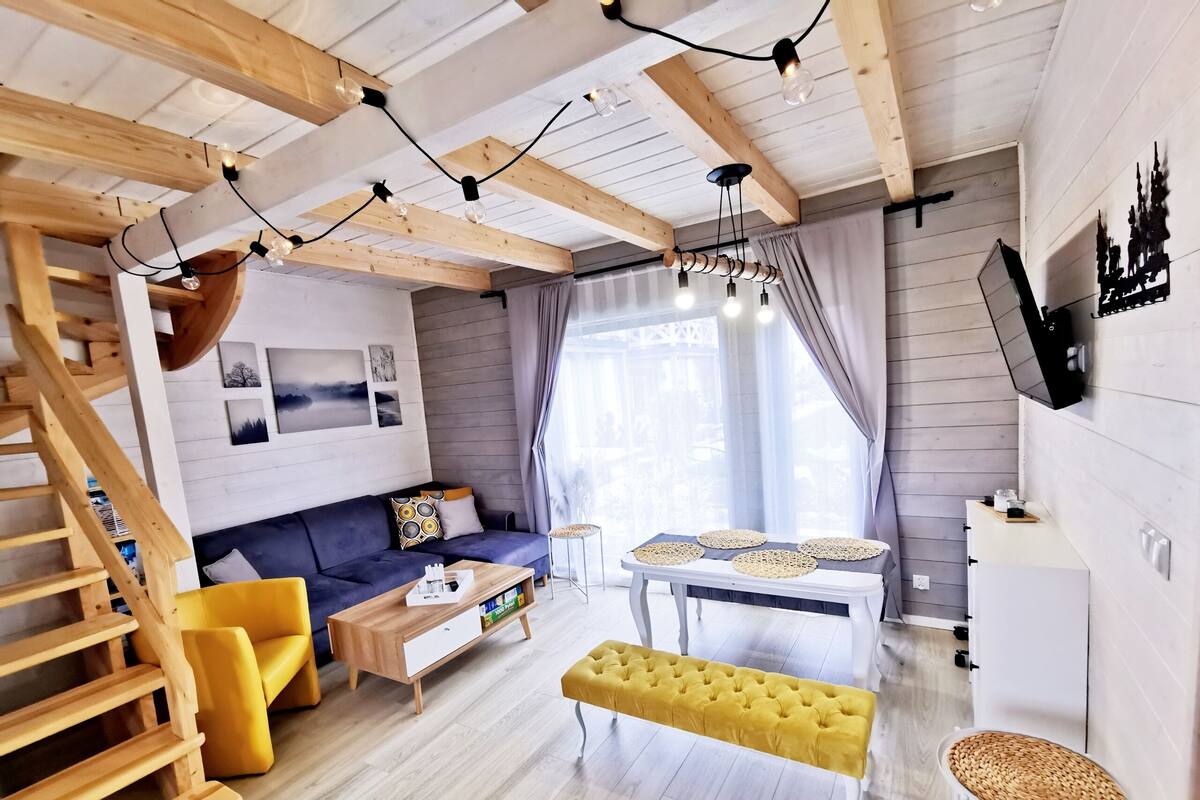 Een moderne woonkamer met een houten trap, een bank, een salontafel, en een eethoek met een tafel en stoelen.