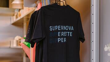 Een zwart T-shirt hangt aan een rek, met de tekst 'SUPERNOVA SUPERETTE SUPPER' erop.