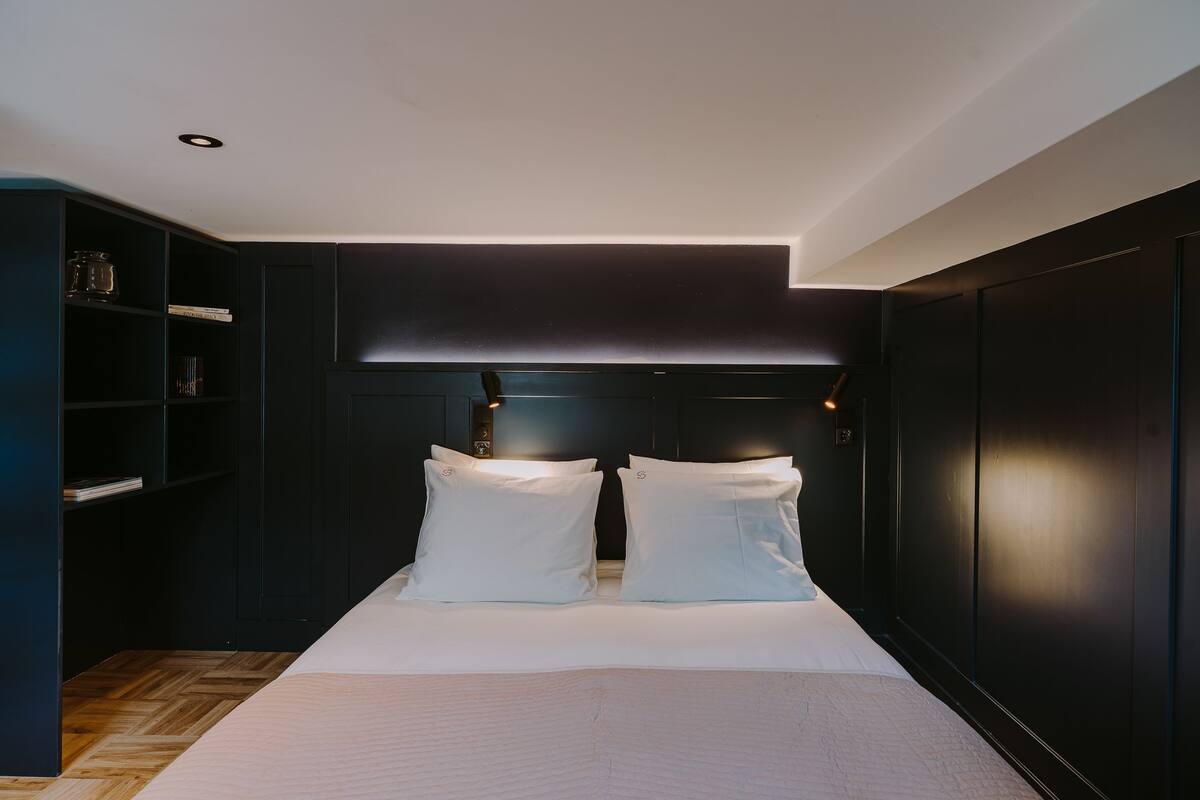 Ein modernes Schlafzimmer mit dunklem Kopfteil, Holzboden und einer eingebauten Bücherreoliste.