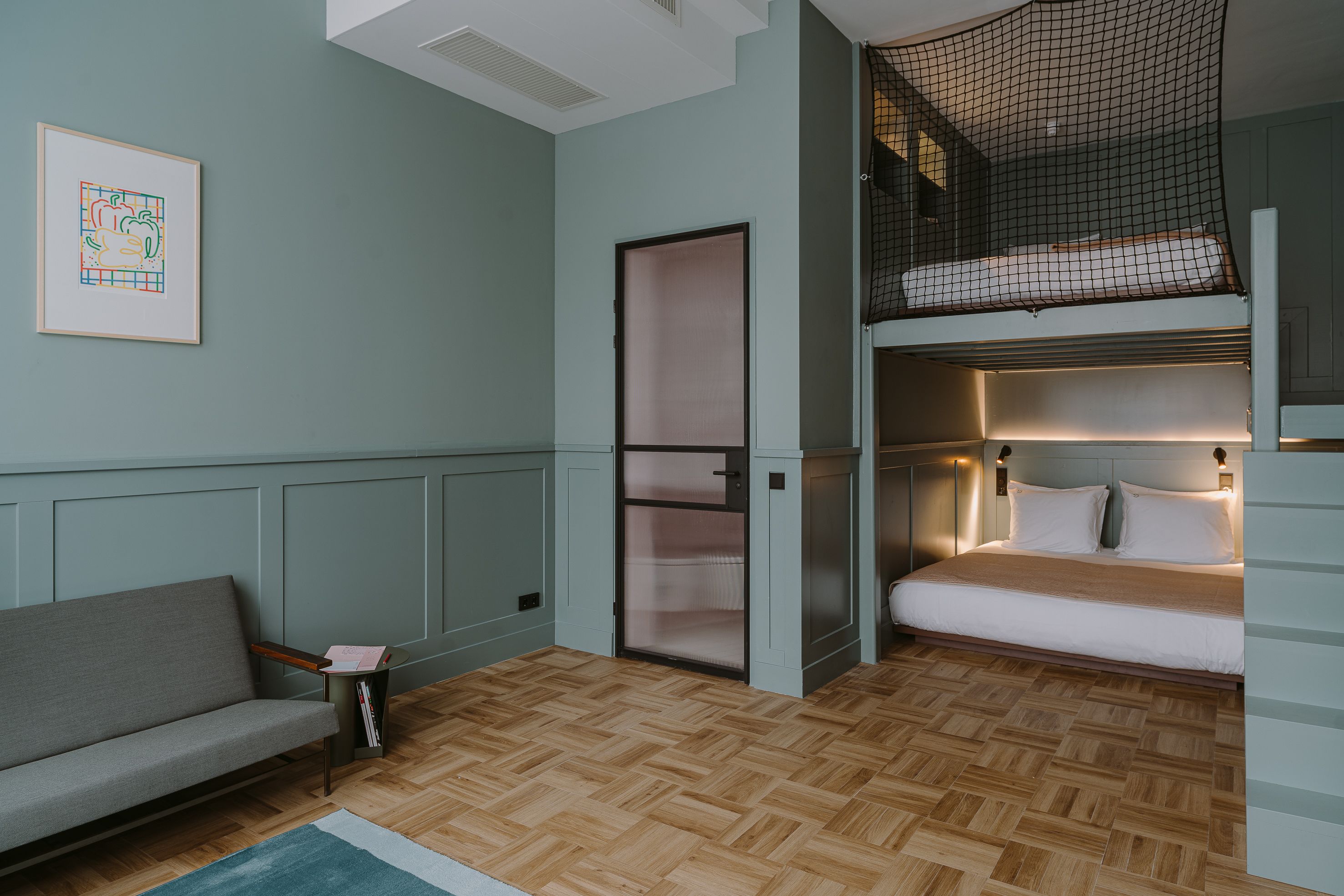 A room with a bunk bed, a sofa, a door, and a framed picture on the wall.
