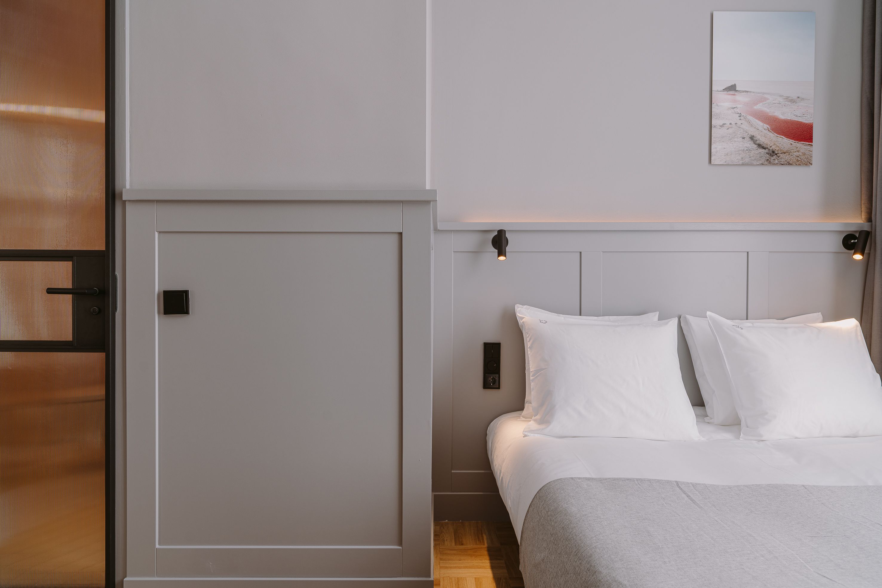 Un dormitorio con cama, paredes blancas, una puerta y un cuadro en la pared.