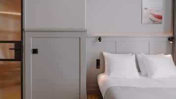 Un dormitorio con cama, paredes blancas, una puerta y un cuadro en la pared.