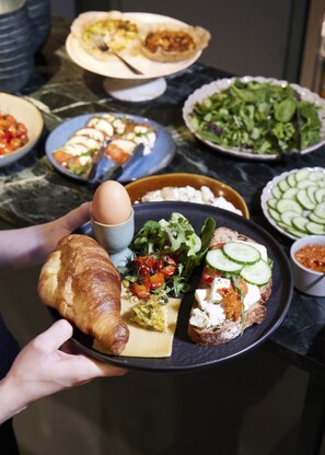 A person holding a tray with a croissant, cheese, and a salad. - Supernova Hotel (Rotterdam)