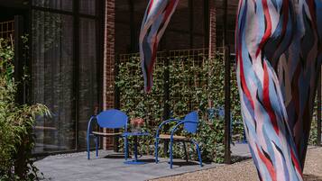 An outdoor seating area with blue chairs and a table, surrounded by a brick wall and greenery.