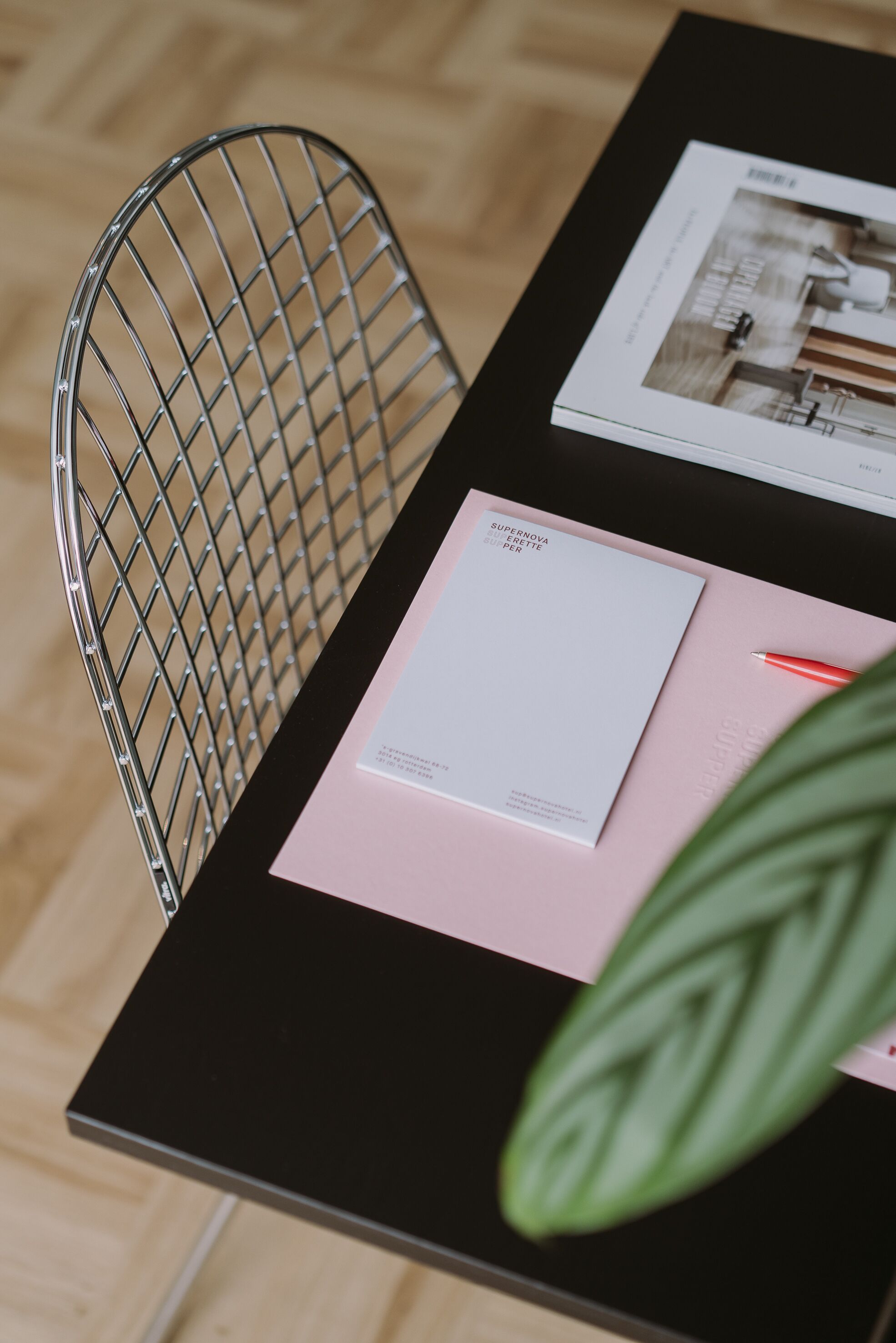 A black table with a metal chair, a pink folder, a white envelope, and a red pen.