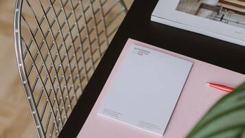 A black table with a metal chair, a pink folder, a white envelope, and a red pen.