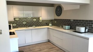 Una cocina moderna con armarios blancos, salpicadero de azulejos negros y verdes, y suelo de madera.