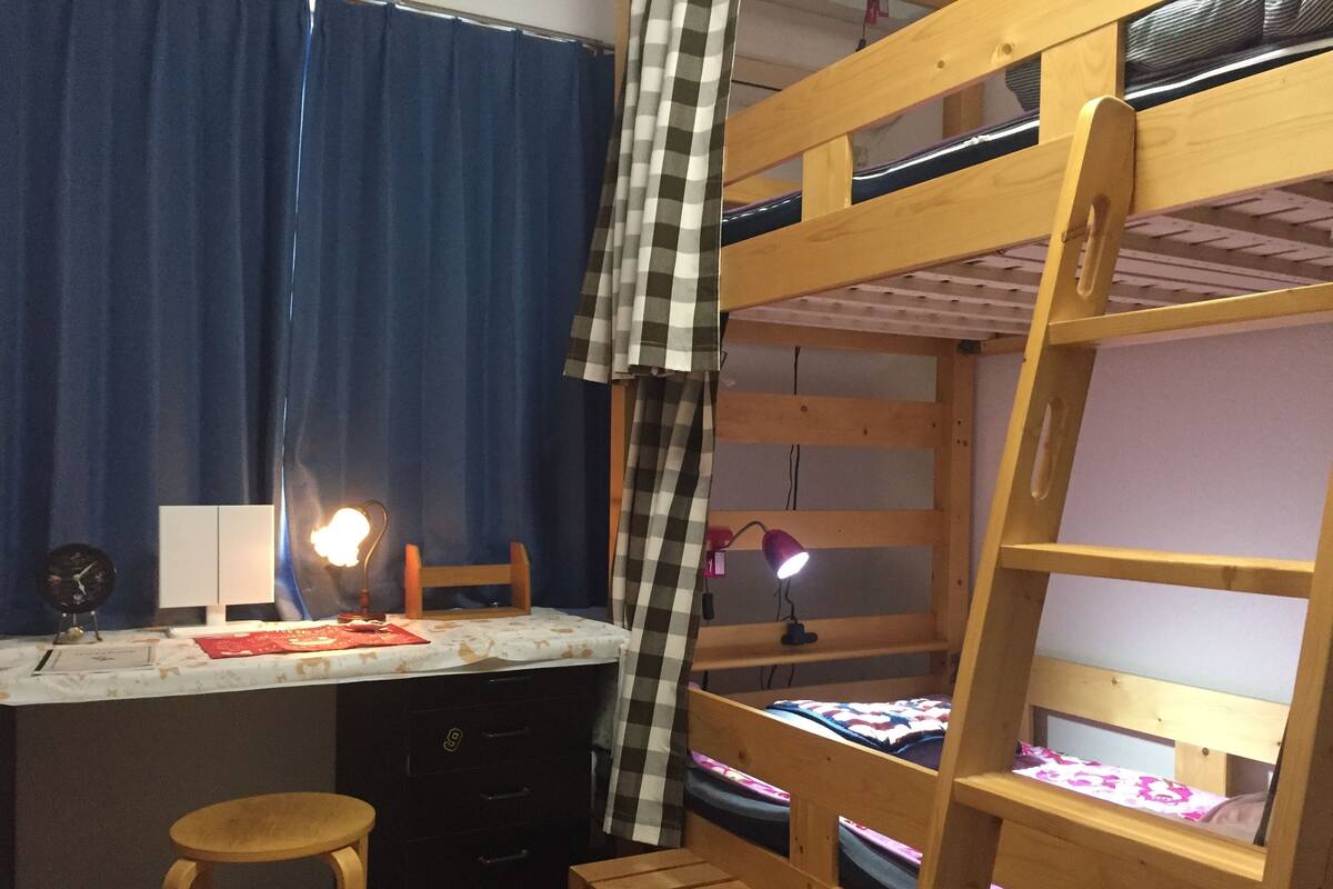 A bunk bed with a desk and two lamps, a chair, and a small stool.