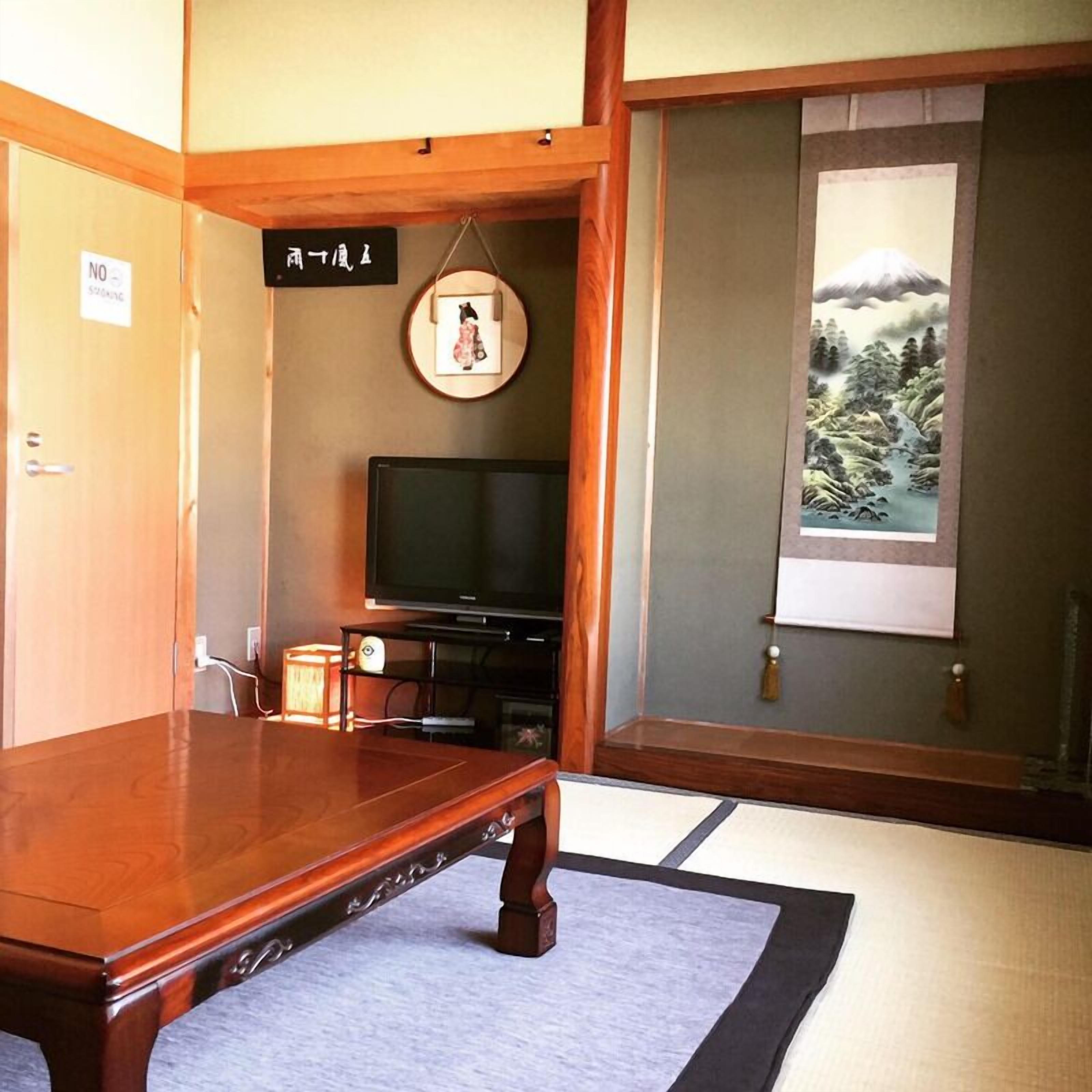 A traditional Japanese room with tatami flooring, a television, a framed picture on the wall, and a view of a mountain through a window.