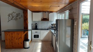 Una cocina compacta con techo de madera, armarios blancos, un refrigerador de acero inoxidable y un microondas.