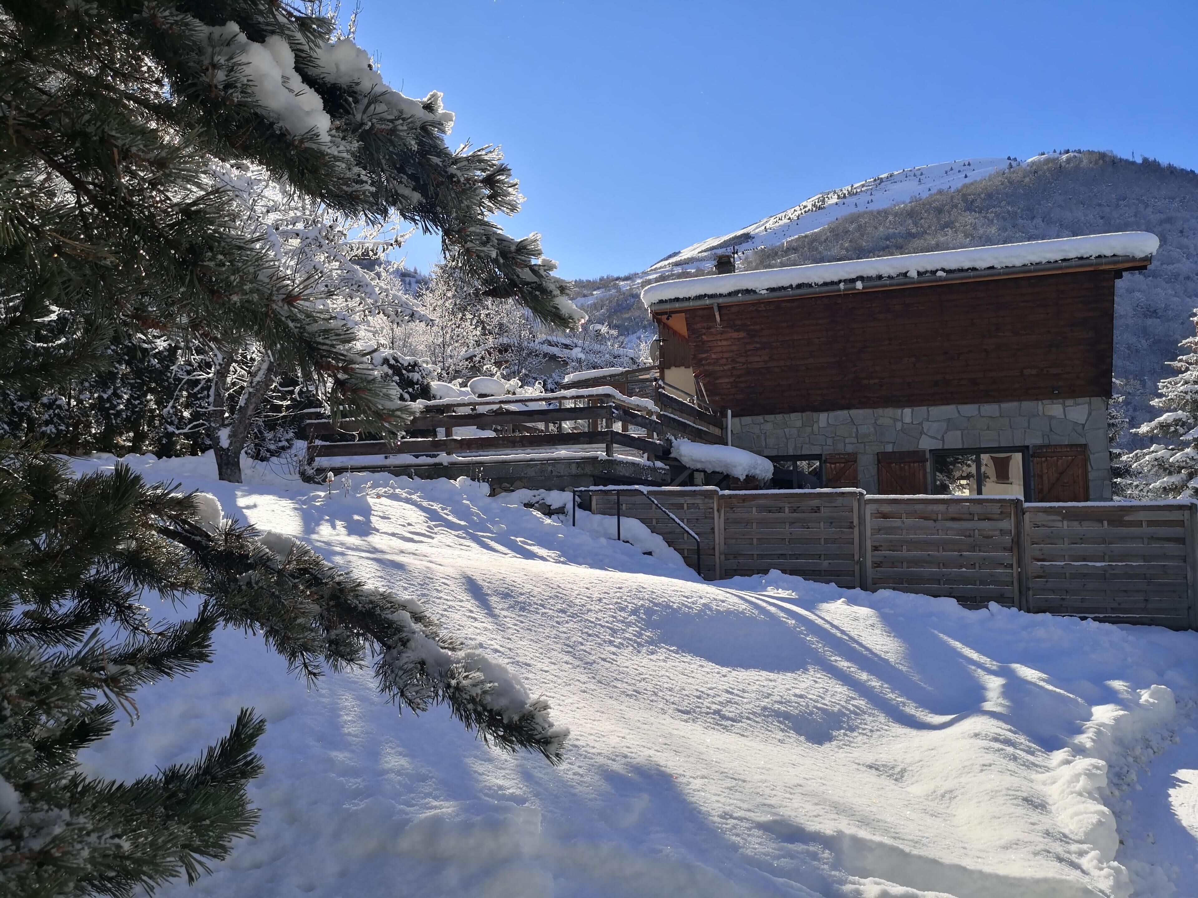 Eine Holzhütte mit Steinverkleidung, umgeben von schneebedeckten Bäumen und einem Berg im Hintergrund.