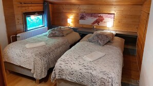 Un dormitorio estilo cabaña acogedor, con dos camas, una ventana, un televisor de pared y un cuadro enmarcado.