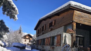 Una cabaña de madera con paredes de piedra, techo cubierto de nieve y una noria grande.