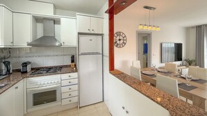 A modern kitchen with white cabinets, a built-in oven, and a refrigerator. There is a dining area with a table and chairs, and a clock on the wall. - Club Villamar - Holiday villa with a beautiful appearance, located at the Spanish Costa Brava. (Lloret de Mar)