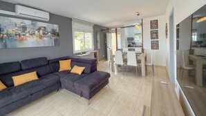 A modern living room with a sectional sofa, dining area, and kitchen visible through an open door. - Club Villamar - Holiday villa with a beautiful appearance, located at the Spanish Costa Brava. (Lloret de Mar)
