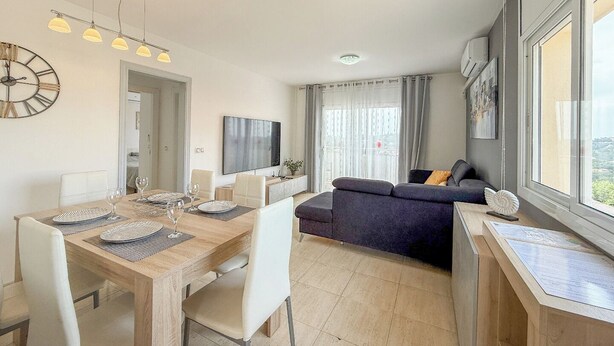 A modern living room with a dining area, a sofa, and a TV. - Club Villamar - Holiday villa with a beautiful appearance, located at the Spanish Costa Brava. (Lloret de Mar)