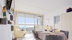 Un espace repas moderne avec une table dressée pour deux personnes, un canapé et une vue sur la mer grâce à de grandes fenêtres.