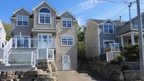 A two-story house with a stone staircase leading to the front door, a small porch with a railing, and a clear sky. - Stunning 1-Bedroom Furnished Apartment Overlooking Beautiful Halifax Harbour (Dartmouth)