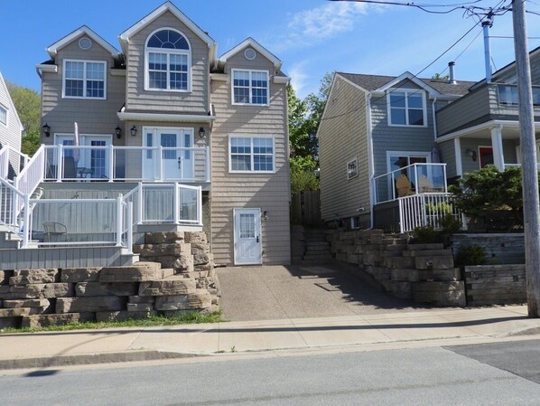 A two-story house with a stone staircase leading to the front door, a small porch with a railing, and a clear sky.