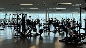 A gym with various exercise machines, large windows, and a ceiling with exposed pipes. - Stunning 1-Bedroom Furnished Apartment Overlooking Beautiful Halifax Harbour (Dartmouth)