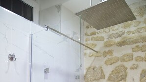 Ducha con cerramiento de vidrio, pared de piedra y azulejos de mármol.