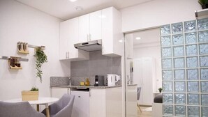 Una cocina compacta con gabinetes blancos, horno integrado y cafetera. Hay un pequeño comedor con mesa y sillas.